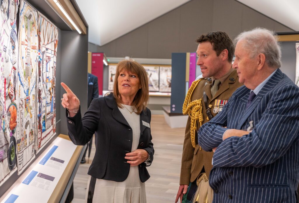 Center Director, Sandy Maxwell-Forbes and King's Equerry, Major Johnny Thompson, view Panel 144, "Pop Music Booms" alongside Alexander McCall Smith